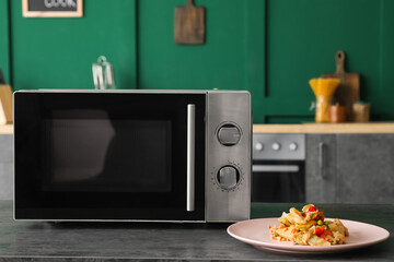 Modern microwave oven and plate with food on table in kitchen