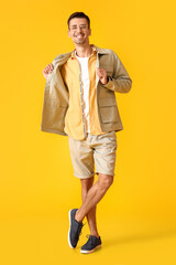 Fototapeta na wymiar Young man in eyeglasses and stylish jacket on yellow background