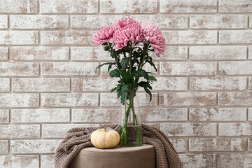 Vase with beautiful chrysanthemum flowers and pumpkin on table against brick wall