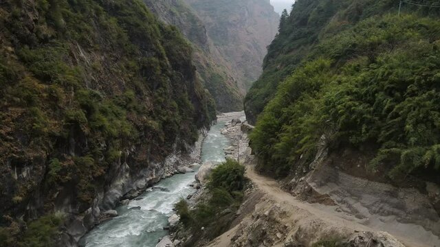 Flying down canyon over the Marsyangdi River viewing dirt road cut into the cliffs in Nepal.