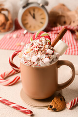 Cup of tasty cacao with candy canes and marshmallows on light background