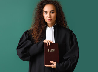 Young female judge with law book on color background