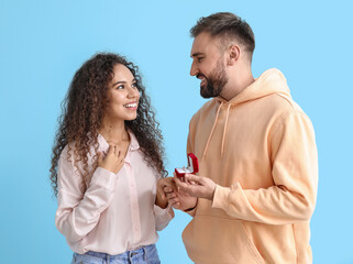 Young man proposing to his girlfriend on color background