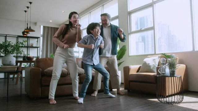 happiness asian family dance along together at home in living room, asian dad mom and son move exercise body weekend morning at home isolation during lockdown period