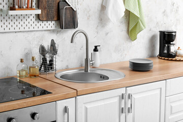 Wooden counter with silver sink and utensils near light wall in kitchen