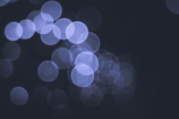 Unfocused bokeh lights in the dark. Abstract background of the lights is out of focus. Colored in trendy color of year 2022 Very Peri. Selective focus, copy space.