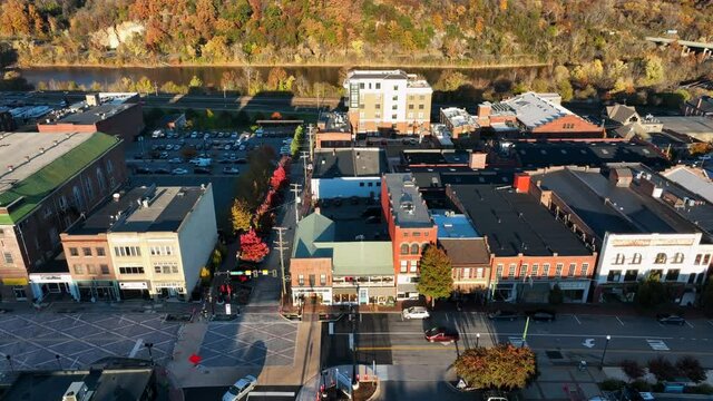Aerial establishing shot of restored storefront businesses in small town America. Golden hour light during colorful autumn foliage. River in distance.
