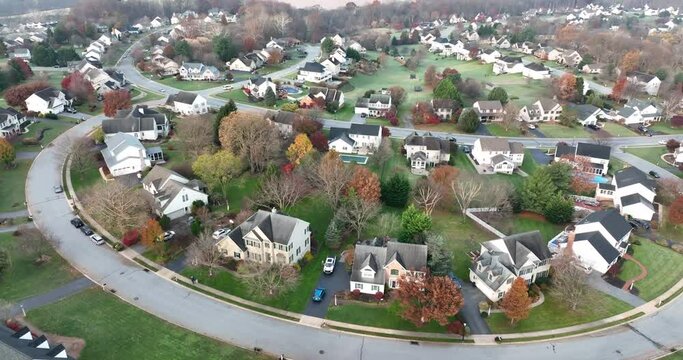 Aerial orbit of residential neighborhood development. Street curves through new homes and houses. Autumn fall morning overcast view.