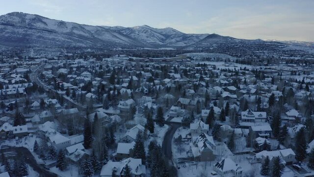 Beautiful aerial drone shot taking houses and roads covered with snow over Park City, Utah,USA in a cold wintry evening.