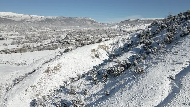 Aerial flight along a frozen hillside toward the town of Eagle with fresh snow during December. Filmed in the Rocky Mountains of Colorado near the town of Eagle along Interstate 70.