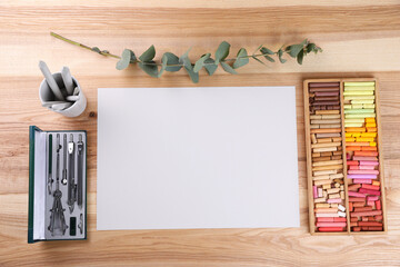 Layout with blank paper, soft pastels and other drawing supplies on wooden table at artist's workplace, top view. Space for design