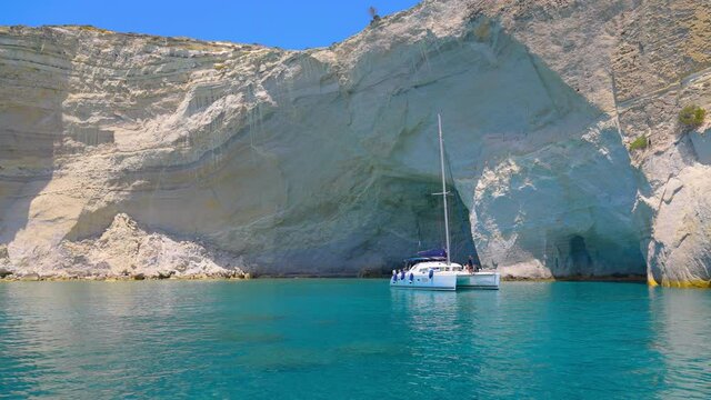 Picturesque Kleftiko Bay on Milos Island, Greece with a catamaran anchored in front of scenic sandstone cliff