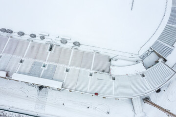 empty football stadium in winter season. stadium seats and soccer field covered with snow. aerial overhead view.
