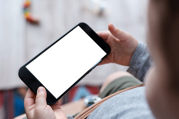 Boy's toddler hands holdingphone on home background. Child's hands hold black smartphone and watching video in horizontal position. Screen blank. Close-Up.