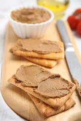 Crispy crackers with delicious meat pate and knife on wooden board, closeup