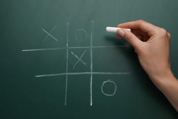 Woman playing tic tac toe game on green chalkboard, top view