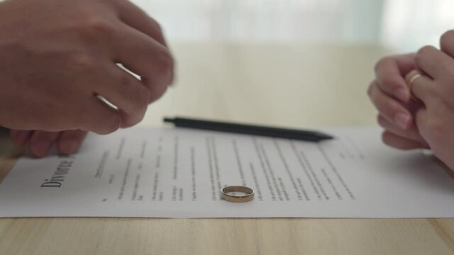 Family conflicts and love problems. The hands of the husband and wife with the divorce paper. The wedding ring was removed on a contract.