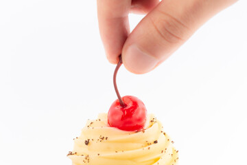 Hand putting a cherry on top of a cup cake icing. Isolated over white background with space for text.