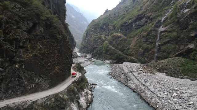 Vehicles driving on narrow cliff road along the Marsyangdi River cut into the mountain side in the wilderness in Nepal.