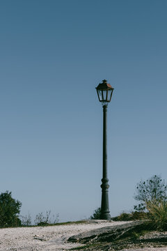 Vertical shot of a street lamp or lantern with a tall pole against the clear blue sky