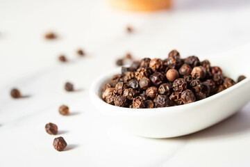 black peppercorns in a spoon on white