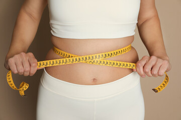 Woman measuring waist with tape on beige background, closeup