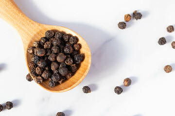 black peppercorns in a spoon on white