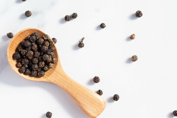 black peppercorns in a spoon on white