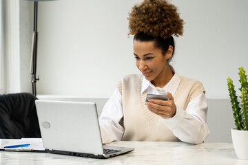 African-American woman holding a credit card, sitting at a table with a laptop, shopping online, making Internet payments
