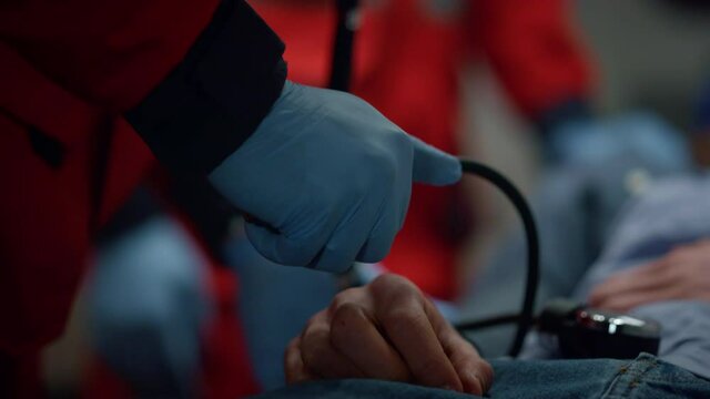 Paramedic hands in gloves measuring patient blood pressure with tonometer