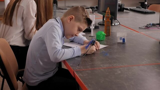 A child, teen boy makes a plastic boat, draws its parts with a 3D pen. A child draws with a 3d pen while sitting at a table in a robotics school.