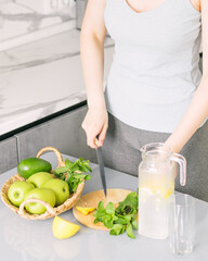 Woman in sportswear makes detox drink with lemon mint in kitchen at home. Rejuvenating invigorating water lemon,