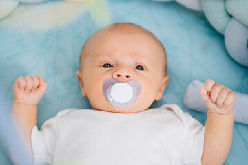 a baby with a pacifier in his mouth lies on a blue diaper. 