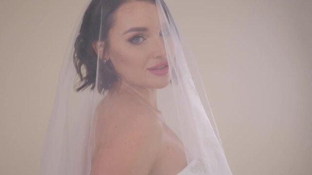 Close-up portrait of a young beautiful bride with dark hair with a head covered with a veil on a white background.