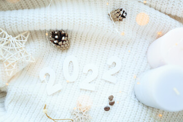 Obraz na płótnie Canvas The number 2022 of bokeh in the house on the table with a sweater in the background and decorations. Winter mood, festive decoration, magical Christmas.