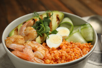 Delicious lentil bowl with avocado, shrimps, egg and cucumber on table, closeup