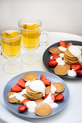 Mini pancakes with sour cream sauce and strawberries on plates, breakfast for the family. Front view.