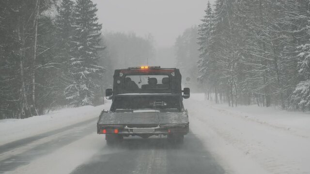 Tow truck with flashing special signal is driving on winter road during snowstorm