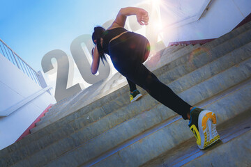 Silhouette of young woman running sprinting up stairs. Fit runner fitness runner during outdoor workout with 2022 text at top of stairs. 2022 time to start running concept.