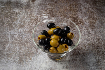 Olives and olives in a glass against the background of a gray stone table.