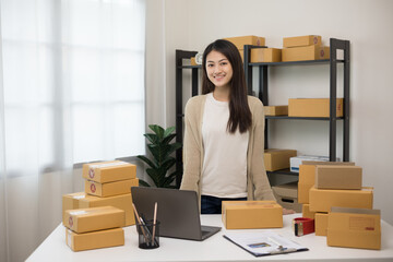 Beautiful young asian entrepreneur standing pose smiling to camera. Female small Business owner with box working at home. Startup freelance people with many parcel on background.