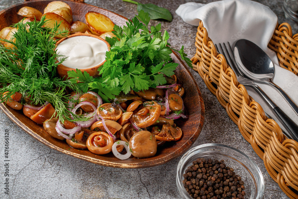 Wall mural Serving a dish from a restaurant menu: country-style baked potatoes with pickled mushrooms and onions, cream sauce, dill and parsley greens on a plate against the background of a gray stone table - Wall murals