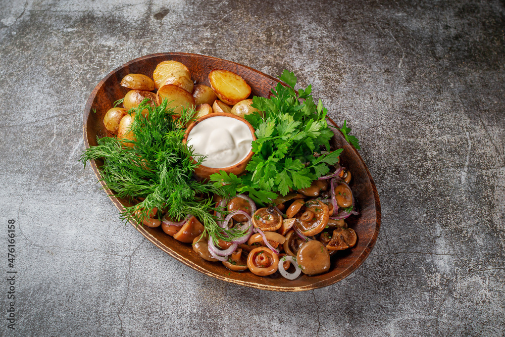 Poster Serving a dish from a restaurant menu: country-style baked potatoes with pickled mushrooms and onions, cream sauce, dill and parsley greens on a plate against the background of a gray stone table - Posters