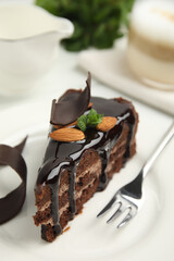 Piece of tasty homemade chocolate cake with mint and almonds on plate, closeup