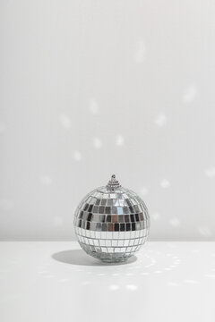 Silver disco ball reflects sunlight on silver background.