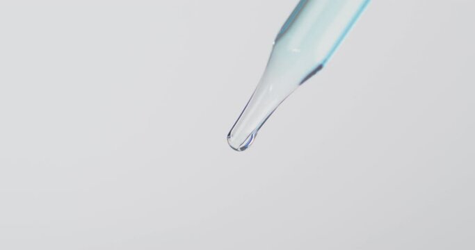 Clear dropper with light blue liquid hanging in drops from the end.
