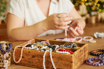 Close-up of a box with jewelry made from semi-precious stones, hands of the master in the background, selective focus