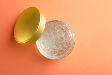 Jar of cosmetic gel on pale orange background, top view. Space for text