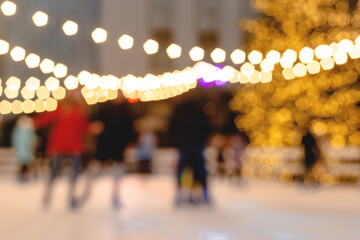 People ride skating rink on background of christmas tree in light garland. Blurred image. Wallpaper