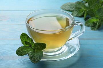 Cup of hot aromatic mint tea on light blue wooden table